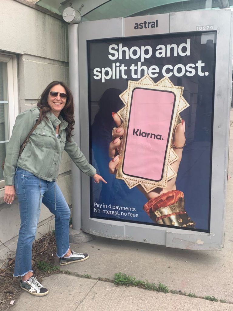Robin standing in front of an ad on a bus stop for a Buy Now Pay Later app called Klarna