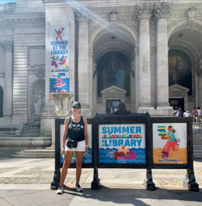 Robin in front of the New York Public Library, with a poster advertising summer reading.