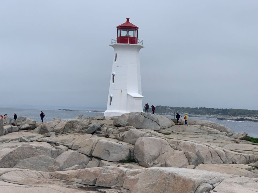 A picture of a lighthouse on the top of some tanned rocks in Nova Scotia. The caption describes how travelling makes Robin happy. 