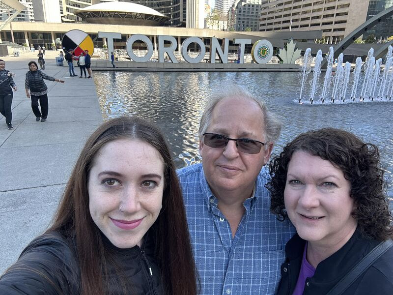 Media and Marketing Manager Lauren Robilliard with her parents in front of a large sign that spells out Toronto.